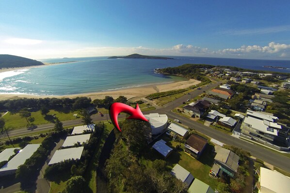 A coastal residential area with a beach, houses, and a large red sculpture.