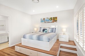 A bedroom with a bed, a nightstand, a dresser, and a staircase.