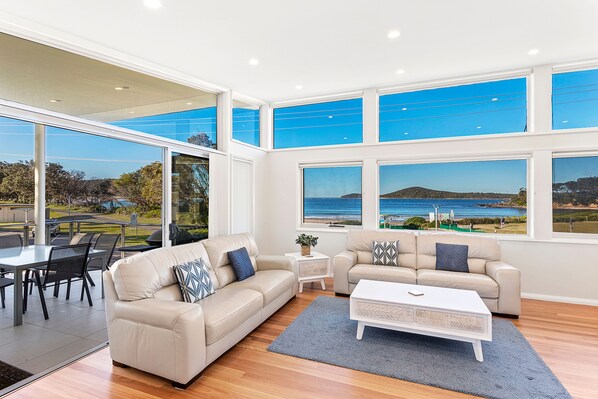 A spacious living area with a large window overlooking a scenic landscape. - Serenity 1 at Fingal Bay with Ocean Views (Fingal Bay)