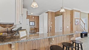 A kitchen with wooden paneling, granite countertops, pendant lighting, and a built-in island with stools. - Oceanfront retreat in Holden Beach, 4BR, 3BA, sleeps 10 with stunning views! (Holden Beach)