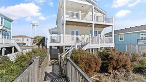 A multi-story house with a balcony, a staircase, and a water tower in the background. - Oceanfront retreat in Holden Beach, 4BR, 3BA, sleeps 10 with stunning views! (Holden Beach)