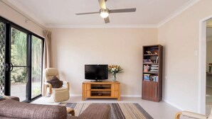 Ein Wohnzimmer mit Fernseher, Bücherregal und Deckenventilator.