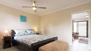 Ein Schlafzimmer mit einem Bett, Nachttischen, einer Bank, einem Deckenventilator und Blick auf einen Balkon.