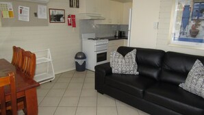 Un espace de vie compact comprenant un coin repas, un canapé en cuir noir agrémenté de coussins à motifs, une cuisine avec des appareils électroménagers blancs et un sol carrelé.