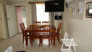 Un coin repas avec une table et des chaises en bois, un téléviseur fixé au mur et un réfrigérateur blanc.