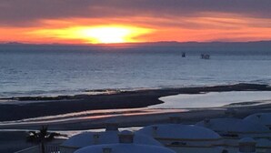 Solnedgang over vand med en strand og kuppelformede bygninger i forgrunden.