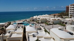 Et resort med flere bygninger med hvide tage, en swimmingpool og udsigt til stranden.