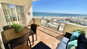 En balkon med udsigt over stranden, et bord med en plante og en sofa med puder.