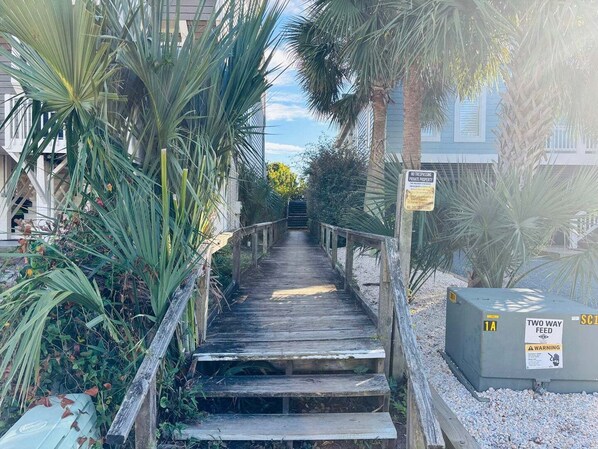 A wooden staircase leading to a gated area with a 'NO TRESPASSING' sign, surrounded by palm trees and a two-way feed sign.
