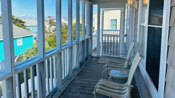 Een overdekt terras met uitzicht op omliggende huizen, een balustrade en twee stoelen.
