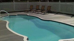 Una piscina con bordo in legno e sdraio.