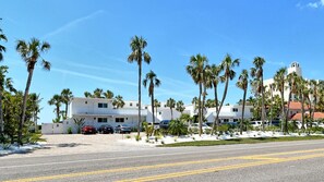 A hotel with a white exterior, multiple floors, and a parking lot with several cars.