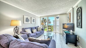 A living room with a sofa, a TV, and a balcony with a view of the sea.