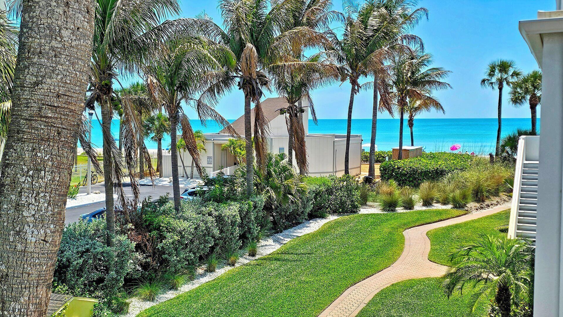 A coastal property with a pathway leading to a beach, surrounded by palm trees and a clear view of the ocean.
