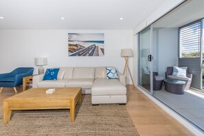 A modern living room with a sofa, a coffee table, and a chair. There is a painting on the wall and a lamp beside the sofa.