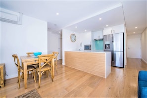 Een moderne keuken met een centraal eiland, roestvrijstalen apparatuur en een eethoek met houten meubels.