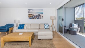 A modern living room with a sofa, coffee table, and a painting of a beach scene. - Beautiful water views of Shoal Bay (Shoal Bay)