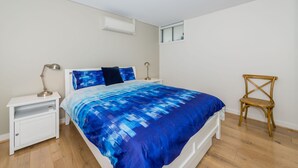 Quarto com cama, mesas de cabeceira, uma cadeira, janela e ar condicionado.