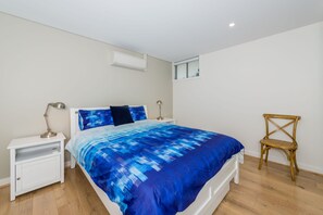 Een slaapkamer met een bed, nachtkastjes, een stoel, een raam en een airconditioning.