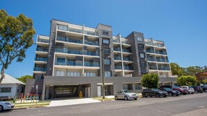 Um edifício residencial com vários andares, varandas, área de estacionamento e céu claro.