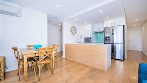 A modern kitchen with a wooden dining table, chairs, a built-in island, and a stainless steel refrigerator. - Beautiful water views of Shoal Bay (Shoal Bay)