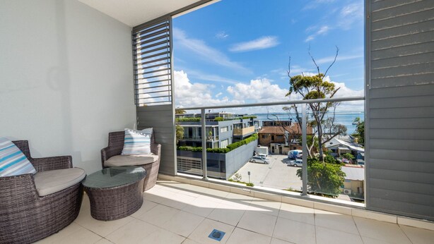 A balcony with wicker furniture, a glass table, and a view of a residential area and the sea. - Beautiful water views of Shoal Bay (Shoal Bay)
