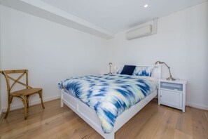 A bedroom with a bed, a chair, a nightstand, and an air conditioning unit.