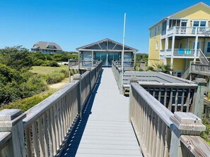 A wooden boardwalk leading to a building with a covered entrance and a flagpole.