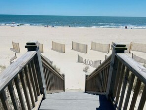 Une promenade en bois mène à une plage de sable, d’où l’on a une vue dégagée sur l’océan.