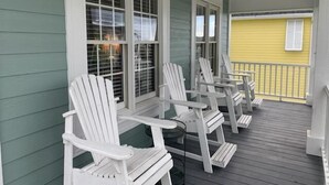 Une véranda avec des fauteuils Adirondack blancs et une terrasse en bois.