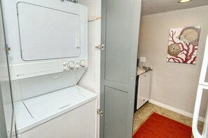 A laundry room with a white washer and dryer, a gray door, and a red rug on the floor.