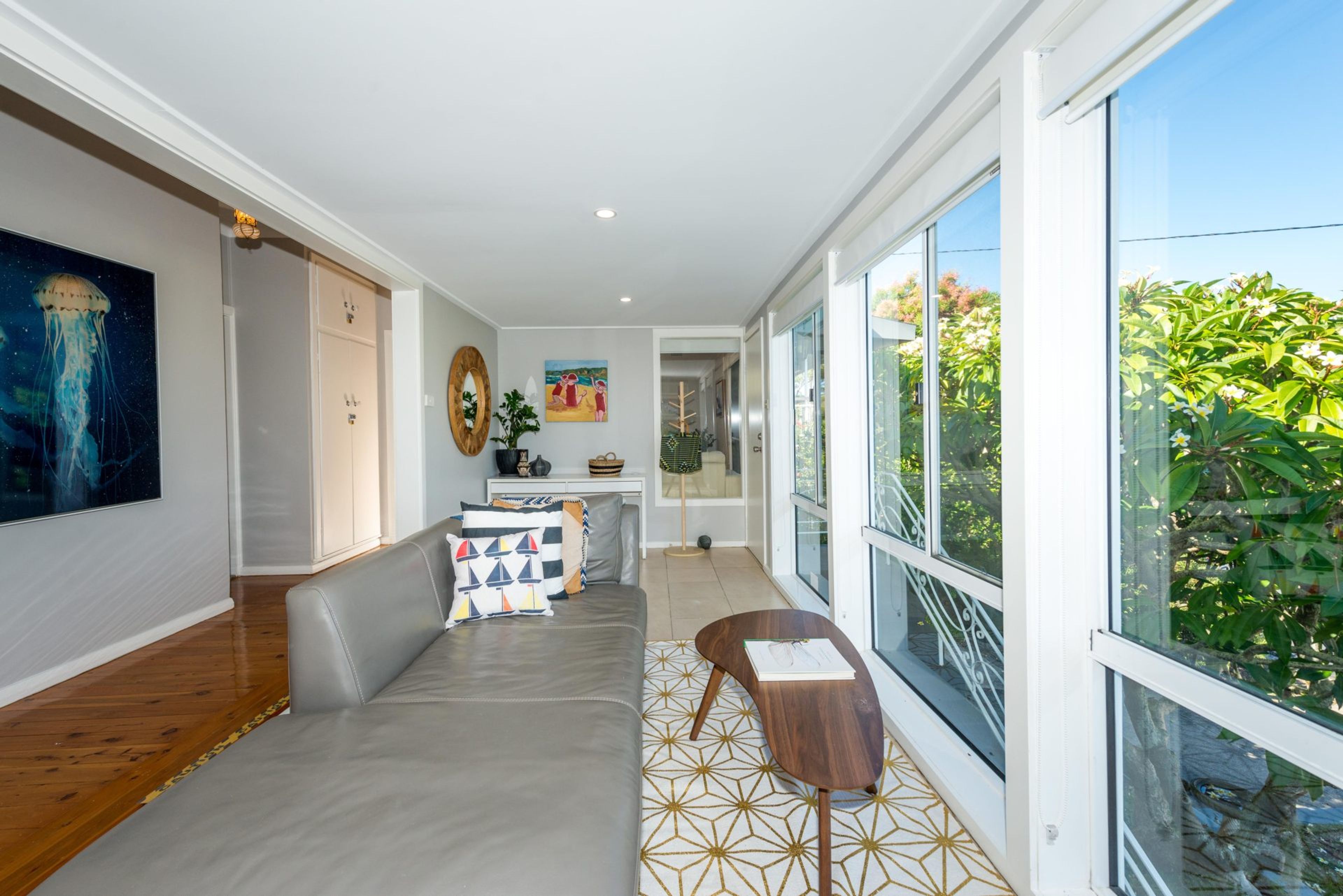 A modern interior with a long hallway, a dining area, and a large window offering a view of greenery.