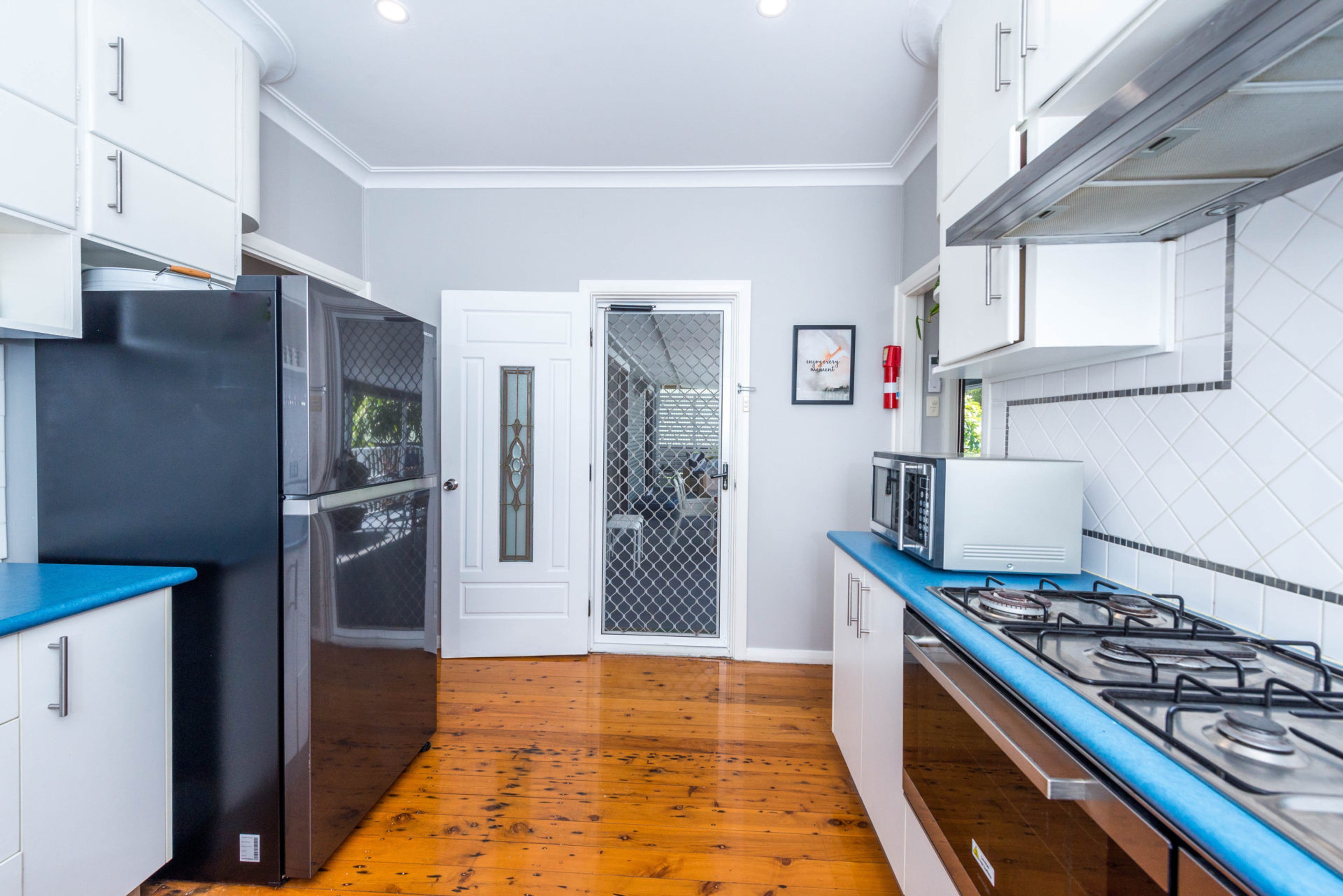 Une cuisine moderne avec des meubles blancs, un réfrigérateur noir, un four à micro-ondes et une cuisinière à gaz.
