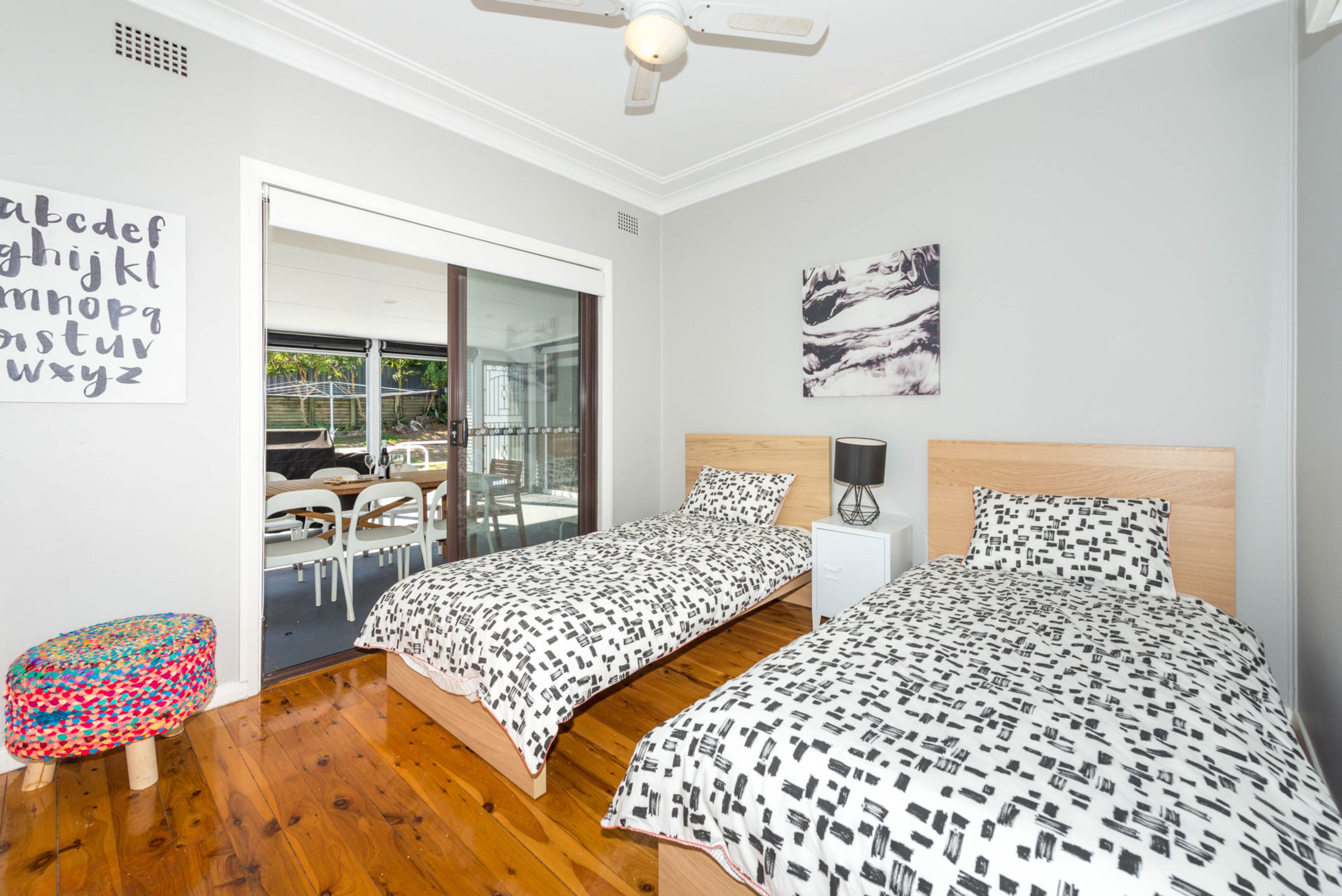 Une chambre avec deux lits, une petite table, une chaise et un ventilateur de plafond.
