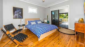 A bedroom with a bed, a chair, a small table, a ceiling fan, and a window. - Victor Parade Pet Friendly Shoal Bay Home (Shoal Bay)