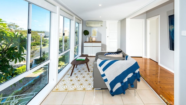 A modern living room with a sofa, a small table, and a view through large windows. - Victor Parade Pet Friendly Shoal Bay Home (Shoal Bay)