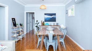 Een eetgedeelte met een houten tafel en metalen stoelen, een boekenkast en een aan de muur hangend schilderij.