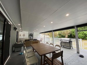 Een terras buiten met een houten tafel en stoelen, een barbecue en een overdekte zithoek.