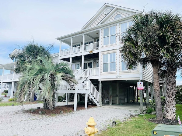 Une maison à deux étages située en bord de mer, dotée d’un balcon, de palmiers et d’un potelet d’hydrant jaune.