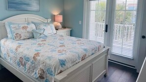 Een slaapkamer met een bed, nachtkastje, lamp, raam met jaloezieën en een plafondventilator.