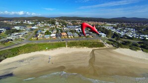 Luchtbeeld van een kustgebied met een groot rood sculptuur, woongebouwen en een zandstrand.