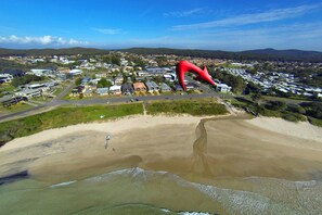 Vista aérea de uma área costeira com uma grande escultura vermelha, edifícios residenciais e uma praia de areia.