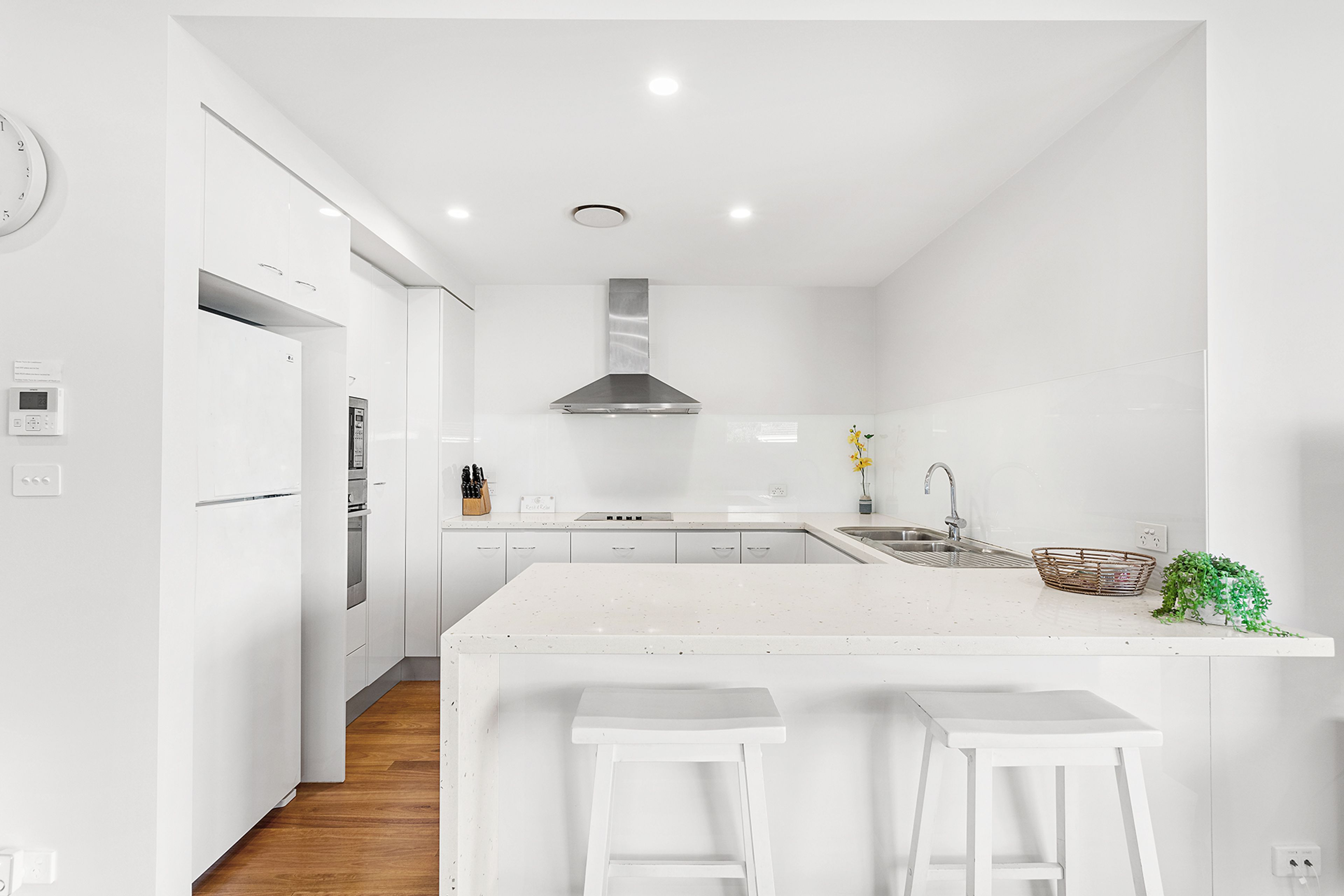 A modern kitchen with white cabinetry, a stainless steel range hood, a built-in oven, and a large island with bar stools.