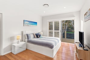 A bedroom with a bed, bedside tables, a TV, and a window with blinds. - Serenity 2 at Fingal Bay Waterfront Family Home (Fingal Bay)