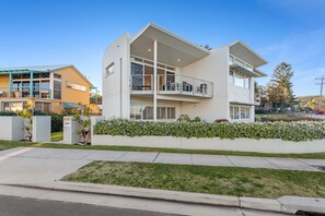 A modern two-story residential building with a flat roof, large windows, and a balcony.