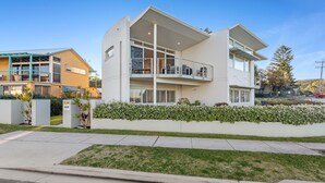 Ein modernes, zweistöckiges Haus mit Balkon, einem gepflegten Rasen und einem Nachbargebäude.