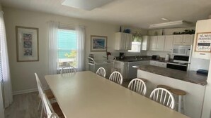 Una cocina amplia con armarios blancos, una mesa de comedor con sillas y vistas al exterior a través del ventanal.