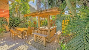 A wooden deck with a pergola, surrounded by tropical plants and a house in the background. - Gertrude's Siesta | 4-min Walk to Beach & Village | Balcony & Tropical Patio! (Siesta Key)