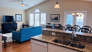 A modern kitchen with granite countertops, a dishwasher, and a dining area with chairs. - Stay at Wolfpack Waves, a spacious 4BR home in Holden Beach, perfect for 10 guests! (Holden Beach)