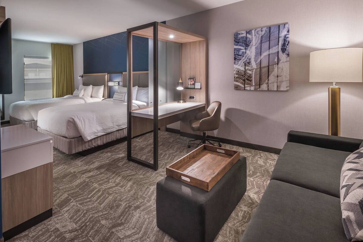 A hotel room with two beds, a desk, a chair, a sofa, a wooden tray, and a large mirror.